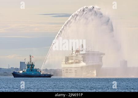 The escort tug Phenix provides a water salute for the Cunard ocean liner Queen Mary 2 on Southampton Water - May 2022. Stock Photo