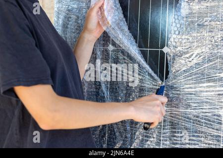 Close up view of unrecognizable young working woman unwrapping a photovoltaic panel with a cutter Stock Photo