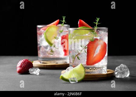 Fresh strawberry mojito cocktail. Two glasses with cold summer strawberry soda drink with strawberry, ice cubes and lime, decorated wiht thyme on dark Stock Photo