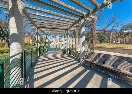 Concrete walkway with pergola and bench near the river at San Antonio, Texas. There is a railings on the left from the river and bench on the right ag Stock Photo