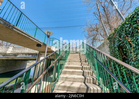 Staircase with metal railings near the river at San Antonio, Texas. Concrete steps leading to a bridge with lamp post on the left near the ramp and a Stock Photo