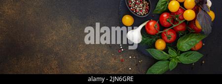 Food banner, fresh ripe red and yellow tomatoes, spices and basil leaves, garlic and green onions on dark board, healthy food concept, copy space Stock Photo