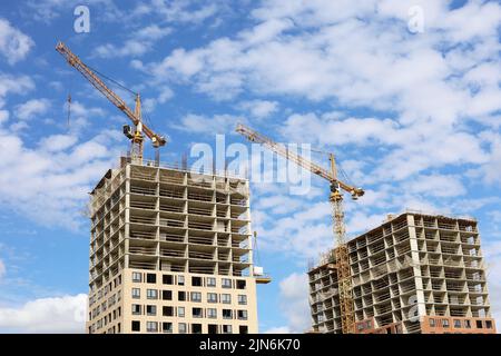 Two tower cranes and unfinished buildings on background of blue sky with white clouds. Housing construction, apartment blocks in city Stock Photo