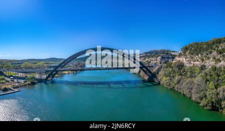 Austin, Texas- Through arch bridge and Colorado River. Bridge connecting the plain land on the left and mountain area on the right against the clear b Stock Photo