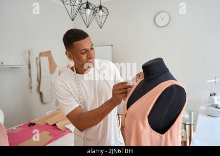 Happy young male fashion designer creating pink dress Stock Photo
