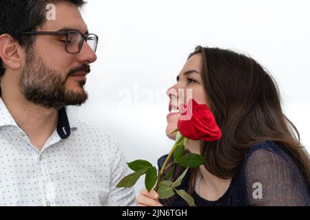 young brown-haired, smiling couple in love looking into each other's eyes with a rose in hand Stock Photo