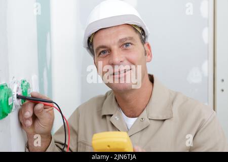 portrait of male electrician using multimeter to test socket Stock Photo