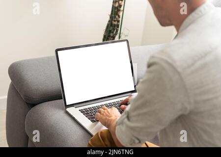 Young male tech user relaxing on sofa holding laptop computer mock up blank white screen. Man using modern notebook surfing internet, read news Stock Photo