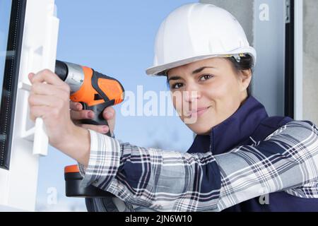 young female builder drilling a hole in a new wall Stock Photo