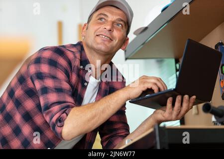 smiling carpenter using laptop at work in workshop Stock Photo