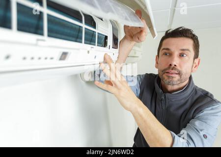 mature male technician fixing air conditioner with screwdriver Stock Photo