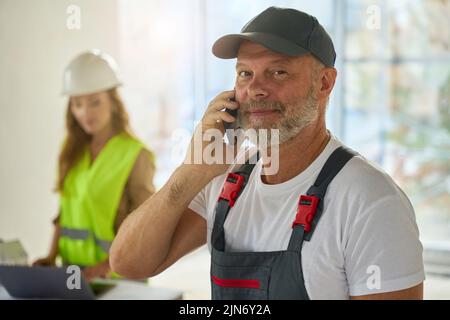 Photo of builder talking on phone. In background is realtor Stock Photo