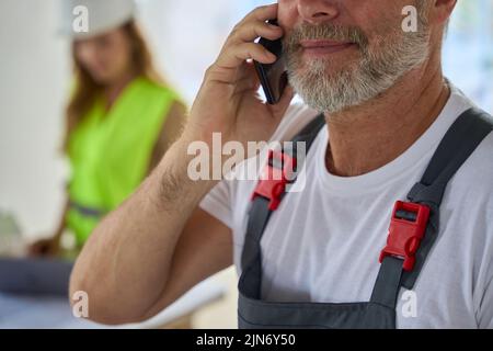 Close-up face of builder with phone. Behind him stands manager Stock Photo