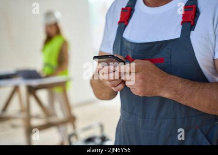 Cropped photo of construction worker typing message on phone Stock Photo