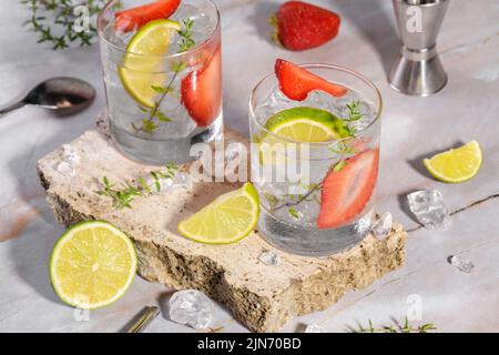 Cold summer strawberry cocktail mojito, margarita, daiquiri. Two glasses with fresh strawberry soda drink, ice and bartender tools on travertine podiu Stock Photo
