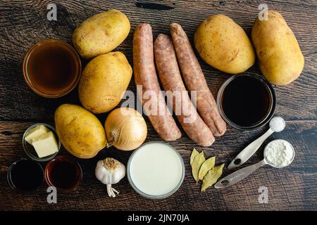 Overhead View of Ingredients for Bangers and Mash with Stout and Onion Gravy: Irish sausages, potatoes, and other raw ingredients on a wood background Stock Photo