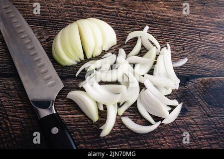 Thinly Sliced Onion on a Dark Wood Cutting Board: Onion sliced into thin wedges with a chef's knife on a wood background Stock Photo