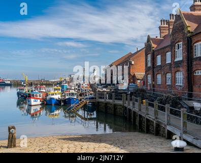 Scarborough, United Kingdom - 16 June, 2022: colorful fishing boats and trawlers next to the red brick harbor building in the marina and port of Scarb Stock Photo