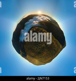 Aerial view from high altitude of little planet earth at sunrise covered with evergreen forest and high mountain peaks Stock Photo