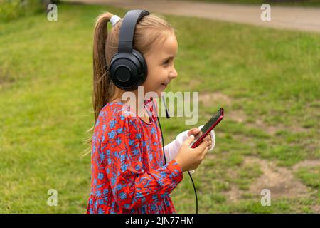 Portrait of caucasian caucasian beautiful girl with mobile phone listening to music in headphones. A beautiful girl holds a mobile phone in her hands Stock Photo