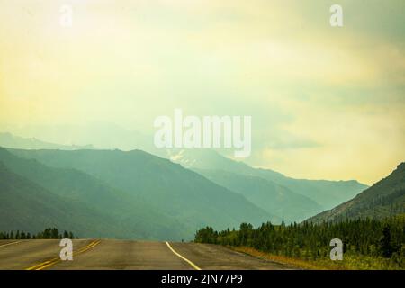 Driving into the misty mountains of Alaska USA near Denali - Two lane blacktop surrounded by pine trees Stock Photo