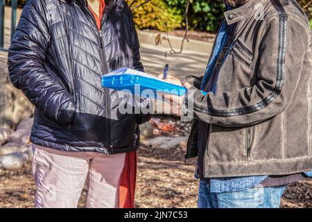 Survey taker talking to another person outdoors and writing answers on cold sunny day - cropped and unrecognizable with blurred background Stock Photo