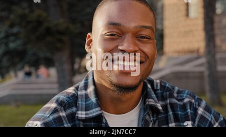Portrait african american happy carefree cheerful smiling man guy looking into distance thinking turns to camera with toothy smile posing outdoors in Stock Photo
