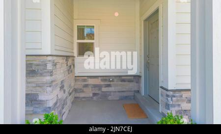 Panorama Entrance of a house with gray door on the side and two potted plants near the column posts. Home exterior with basement windows and white vin Stock Photo