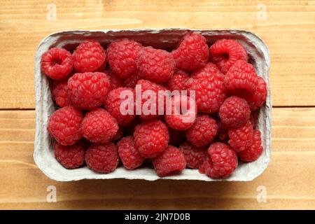 Raspberries are in a cardboard box, which stands on a wooden table. View from above Stock Photo