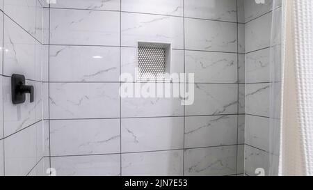 Panorama Shower stall with mosaic tiles flooring and marble tiles surround with black grout. There is a a shower curtain on the left and wall-mounted Stock Photo