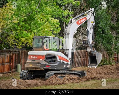 Fort Collins, CO, USA - July 21, 2022: E88, the largest Bobcat compact excavator working in a residential area along backyard fence. Stock Photo
