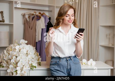 Girl holds a smartphone and a bank card against the background of the wardrobe Stock Photo