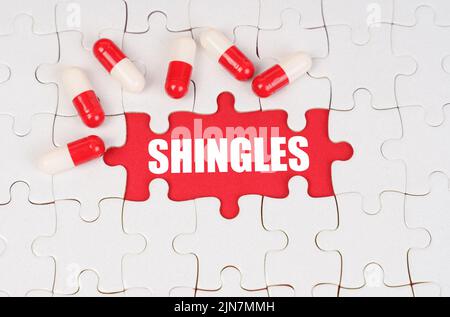 Medical concept. There are pills on the white puzzles, in the middle there is a red surface with the inscription - SHINGLES Stock Photo