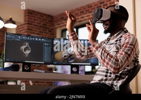 African american developer manufacturing engine gears using vr glasses with 3d simulation and cad software on computer. Techinican developing industrial machinery product with interactive goggles. Stock Photo