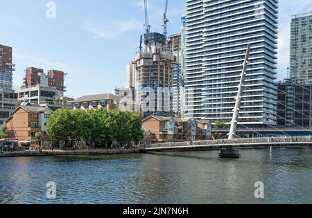 The South Quay Footbridge on a sunny day in Canary Wharf with construction work of new apartment buildings in the distance. London - 9th August 2022 Stock Photo