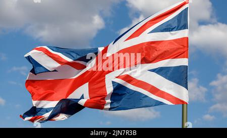 Union Jack flag on a blue sky background futtering in the wind. The flag of the United Kingdom. Stock Photo