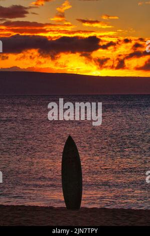 Surf board stuck upright in the sand in silhouette at sunset. Stock Photo