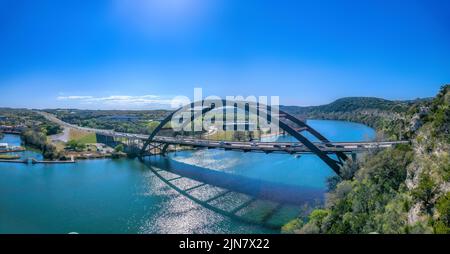 Austin, Texas- Through arch bridge over the Colorado River. Vehicles passing on the large bridge against the view of buildings and clear sky backgroun Stock Photo