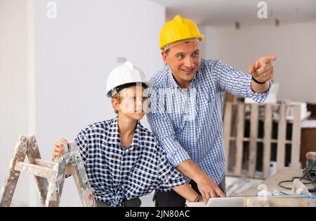 Man architect and boy using laptop while discussing working process in house being renovated Stock Photo