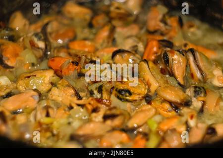 Defocus mussels dish on pan. Delicious seafood mussels with parrot and onion. Heap of peeled mussels with spoon close-up on a dark background. Seafood Stock Photo