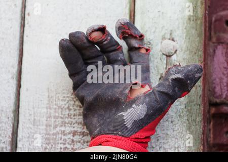 Defocus worn dirty and leaky gloves. Open palms of hands in worn workers gloves, protection against damage during operation, closeup on gray backgroun Stock Photo