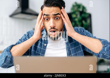 Shocked confused puzzled indian or arabian guy, freelancer or student, looking disappointment at the laptop screen, stressed from the failure of a deal or project, read unexpected news, in desperation Stock Photo