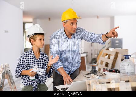 Man architect and boy using laptop while discussing working process in house being renovated Stock Photo