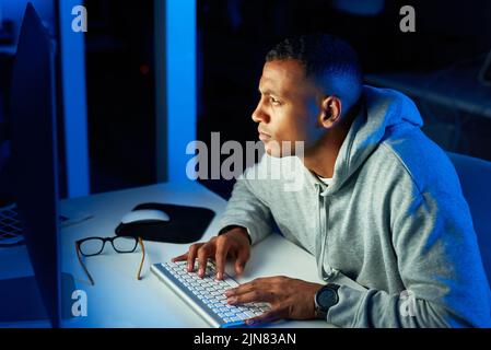 Hes got his eyes on his next victim. a young male hacker cracking a computer code in the dark. Stock Photo