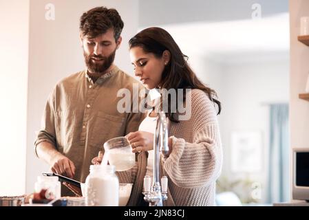 Teamwork makes the batter work. a young couple preparing breakfast at home. Stock Photo