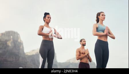 Calm yourselves and storms will pass. a group of young people standing and meditating together while on the beach during an overcast day. Stock Photo
