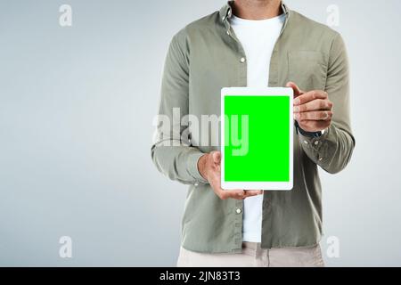 Have a look. an unrecognizable man holding and displaying a digital tablet while standing against a grey background. Stock Photo