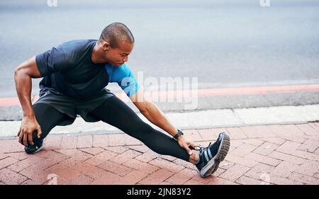 I can never stress the importance of stretching. Full length shot of a handsome young sportsman stretching and warming before exercising outdoors in Stock Photo