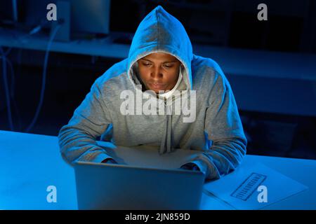 Nothings safe on cyberspace with him around. a young male hacker using a laptop in the dark. Stock Photo