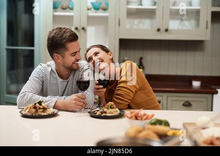 Youre still the best snack. an affectionate young couple smiling at each other while enjoying dinner in their kitchen at home. Stock Photo